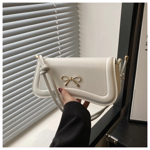 Detailed close-up of a white shoulder bag featuring a decorative golden bow metal clasp