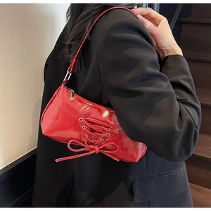 Detail of red patent leather underarm bag with bow ribbons and glossy mirror finish