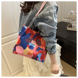 Model wearing a colorful geometric print tote bag with metal chain strap and pink leather detail