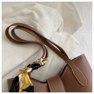 Close-up of brown leather tote bag with contrast stitching and floral silk scarf detail