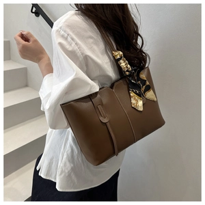 Detail shot of brown leather tote bag with decorative silk scarf on a minimalist staircase