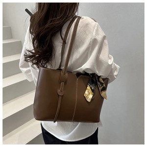Detail of a brown tote bag featuring white stitching and a geometric pattern scarf handle
