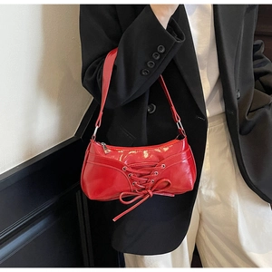 Detail of red glossy shoulder bag with ballet-style corset lacing and bow ribbon
