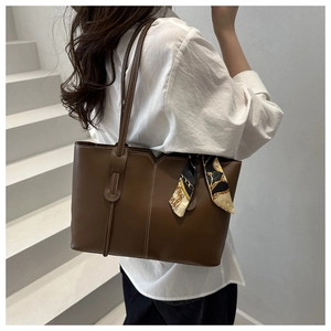 Detail of a large brown leather tote bag with contrast stitching and decorative silk scarf