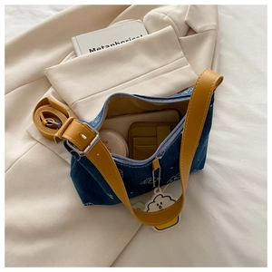 Detail of blue denim shoulder bag with yellow leather strap and white cloud print