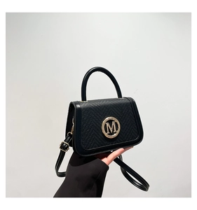 Macro detail of black litchi texture leather bag with gold round M logo buckle