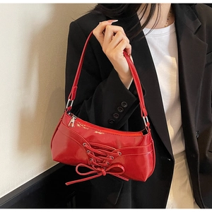 Chic red patent leather underarm bag with decorative bow and criss-cross laces worn by model