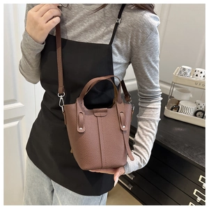 Brown lychee leather bucket bag worn crossbody, showcasing fine texture and silver hardware