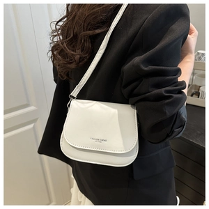 Gros plan d'un sac besace blanc avec logo porté sur un blazer noir par un mannequin