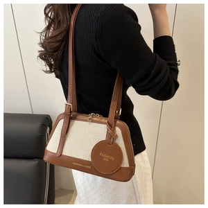 Detail of a brown leather and beige woven shell bag with gold zipper and fashion charm