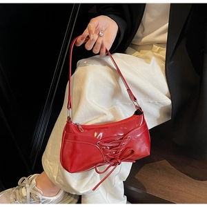 Detail of red glossy patent leather underarm bag with decorative lace-up bow design
