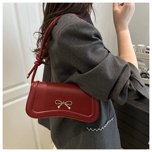 Detail of a dark red matte leather crossbody bag with a gold metal bow and knotted strap