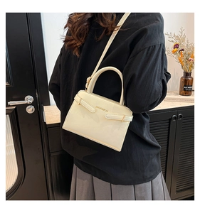 Model met een crèmekleurige vierkante crossbodytas met gespdetail in een gezellige binnenruimte