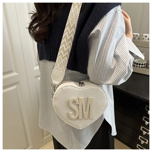 Detail of white heart-shaped leather bag with SM initials and patterned wide strap