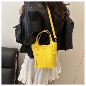 Detailed view of yellow bucket bag in lychee texture worn by a model in a studio