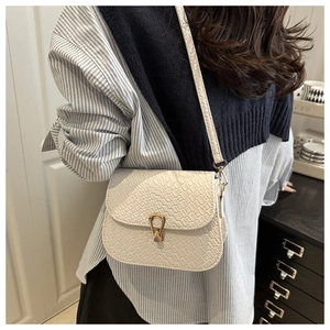 Detail of white woven texture shoulder bag featuring a gold horseshoe clasp on flap