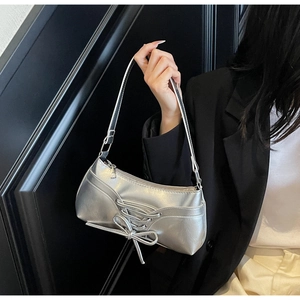 Detail of silver metallic baguette bag with bow and strap worn by a model in black blazer