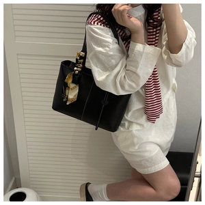 Detail of black leather tote bag with silk scarf on handle held by model in casual suit