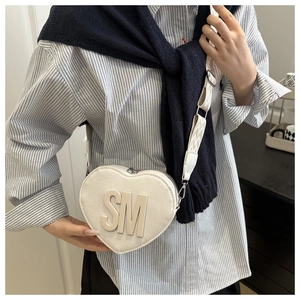 Close-up of white heart-shaped bag featuring textured leather and 3D SM metal lettering