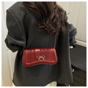 Close-up of wine red crossbody bag with golden bow hardware on gray blazer outfit
