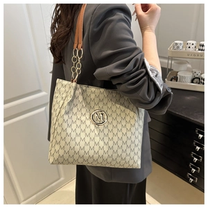 Detailed view of the luxury monogram tote bag featuring a gold metal M logo and leather strap
