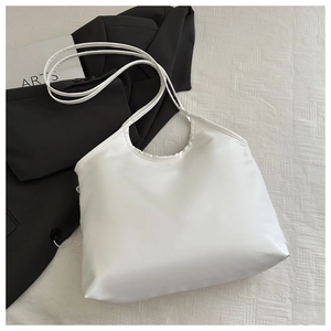 Flat lay of a white glossy tote bag with slender straps on textured fabric backdrop