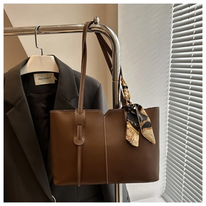 Detail of dark brown tote bag with white stitching and floral scarf on a metal hanger