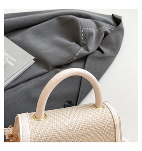 Close-up of beige woven straw handbag with smooth leather handle and gold metal rings