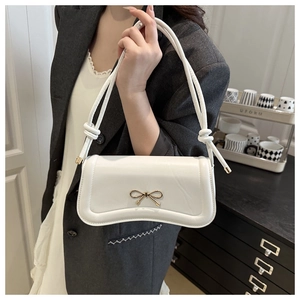 Close-up of a white rectangular handbag featuring a gold bow clasp and knotted rope handle