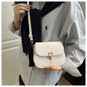 Detail of white crocodile-embossed saddle bag featuring a golden horseshoe metal clasp