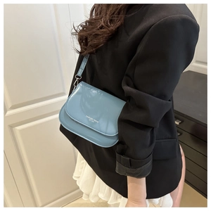 Détail du sac selle en cuir verni bleu clair avec impression de texte tendance