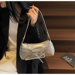 Detail of silver matte underarm bag featuring criss-cross laces and a delicate bow design