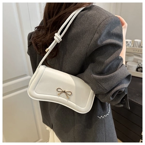 Detailed view of white crossbody bag with gold bow clasp on grey suit model