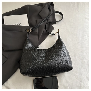 Macro view of black woven embossed underarm bag with phone for scale comparison