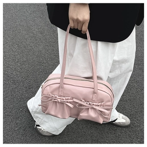 Close-up of pink tote bag featuring bow accents and pleated pockets in street setting