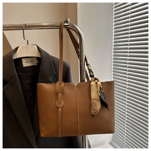Close-up of brown tote bag with decorative silk scarf on handle and sleek stitching