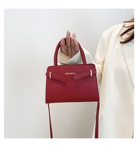 Detailopname van een mat donkerrode leren crossbodytas met chique gouden letterdecoratie