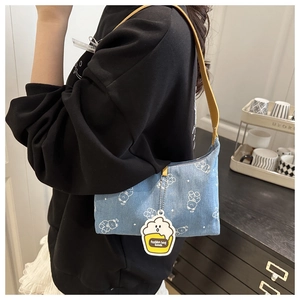 Detail view of denim underarm bag with white bear print and popcorn pendant on shoulder
