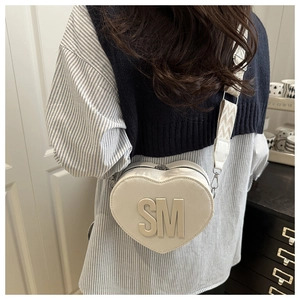 Macro detail of white heart-shaped leather bag with SM logo and wide wavy shoulder strap