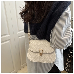 Close-up of a white crossbody bag featuring woven texture and a gold horseshoe buckle