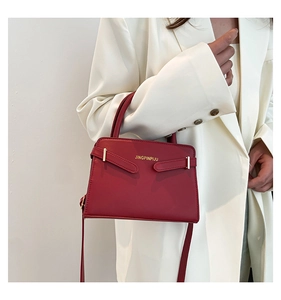 Detail van donkerrode crossbodytas met goudkleurige hardware en handvat voor dames