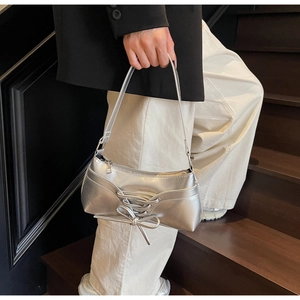 Detail of silver PU leather underarm bag featuring decorative lace-up bow and wavy edge