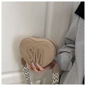 Close-up of heart-shaped beige crossbody bag with SM logo and wave pattern strap