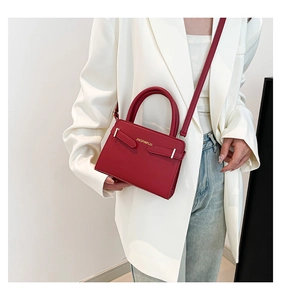 Detail van rode PU-leren handtas met goud logo op witte blazer en spijkerbroek
