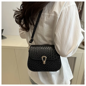 Detail of black crocodile texture shoulder bag with gold horseshoe clasp on white shirt
