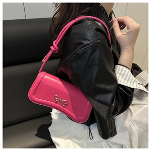 Detail of rose pink baguette bag with golden bow and knot shoulder strap on model
