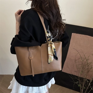 Brown leather tote bag with decorative scarf and tassel shown on model from side-rear angle