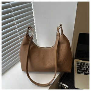 Close-up of brown woven tote bag with leather strap and gold hardware on white ledge