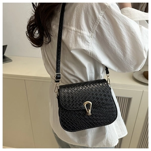 Detail of black crocodile texture crossbody bag with gold horseshoe buckle on white shirt