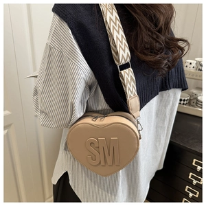 Detail of beige heart-shaped crossbody bag with logo and geometric woven shoulder strap